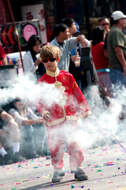 In the minutes leading up to the parade, kids play in the street chasing smoke bombs or streamers shot from cardboard canons.