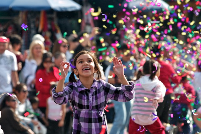 In the minutes leading up to the parade, kids play in the street chasing smoke bombs or streamers shot from cardboard canons.