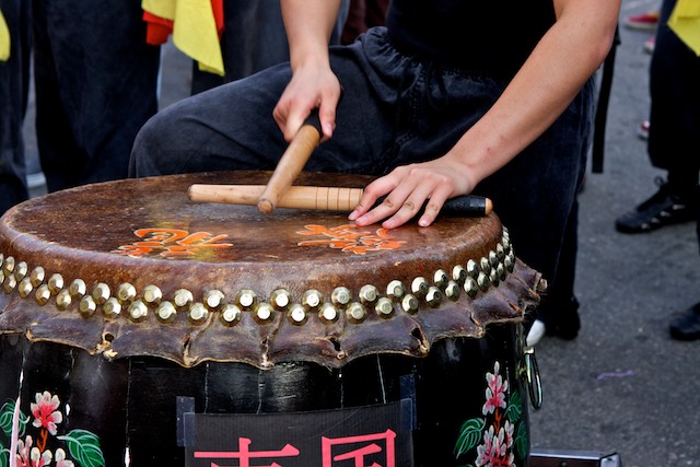 A man from the East Wind troupe plays the drum outside of a restaurant in Chinatown.